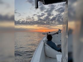A serene sunset view from the deck of a boat, with a guest enjoying the tranquil waters — perfect for unwinding after a day on the sea.