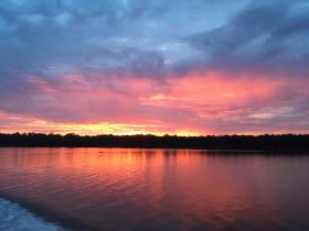 A stunning sunset casts vibrant colors over the water, creating a picturesque reflection — perfect for capturing the beauty of nature during a boating trip.
