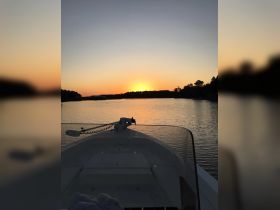 A serene sunset view from the bow of a boat, showcasing the tranquil waters and surrounding landscape — perfect for evening cruises.
