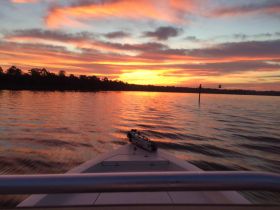 A stunning sunset view from the bow of a boat, showcasing vibrant colors reflecting on the water — perfect for serene evening cruises.