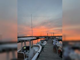 A picturesque sunset over the dock with fishermen preparing their catch, showcasing a serene evening on the water with boats lined up for a perfect fishing experience.