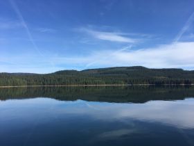 A serene landscape featuring a calm lake surrounded by lush greenery and a clear blue sky, perfect for nature lovers and tranquil escapes.