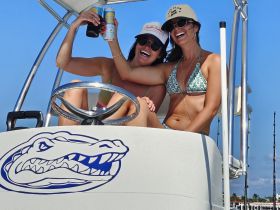 Two friends celebrate on a boat, raising their drinks in a joyful toast under the sun — a perfect moment for fun and relaxation on the water.