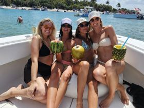 A fun group of friends enjoys refreshing cocktails served in fruit on a boat, perfect for a lively beach day celebration.