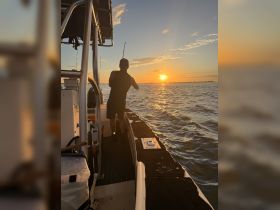 A fisherman casts his line into the shimmering waters at sunset, capturing the essence of a perfect fishing trip on the water.