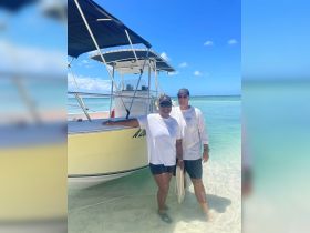 A cheerful couple poses by their boat on a beautiful beach, capturing the essence of a perfect day on the water.