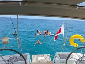 A lively group enjoys a day on the water, paddleboarding and swimming near their boat, capturing the essence of summer fun and adventure.