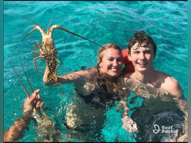 A joyful moment captured as two individuals hold up a lobster while swimming in crystal-clear waters, showcasing a fun underwater adventure.