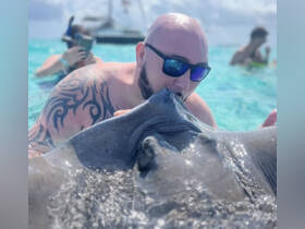 A man interacts closely with a stingray in shallow waters, showcasing a unique wildlife experience — perfect for adventure seekers and marine life enthusiasts.