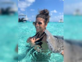 A joyful woman interacts with a stingray in the clear turquoise waters, showcasing a memorable wildlife experience in a tropical paradise.