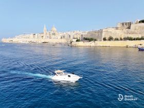 A sleek speedboat navigates the azure waters near the historic skyline of Valletta, Malta, showcasing the beauty of the Mediterranean coast.