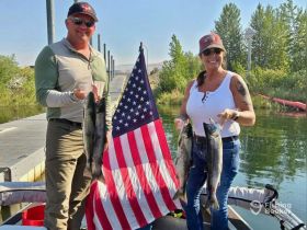 A joyful couple proudly displays their catch of the day while fishing on a boat, showcasing the thrill of outdoor adventures and successful fishing trips.