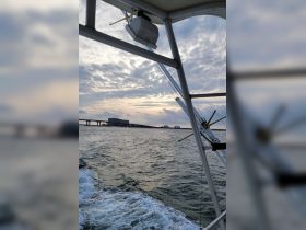 A view from the helm of a boat, showcasing the vessel's structure and the scenic backdrop of a bridge and cloudy sky, perfect for maritime enthusiasts.
