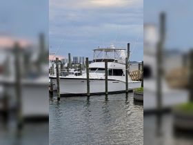 A sleek yacht docked at the marina, showcasing its elegant design against a backdrop of calm waters and distant buildings.