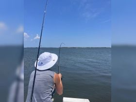A person enjoys a fishing experience on the water, showcasing the thrill of reeling in a catch under a clear blue sky.