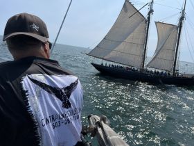 A sailor enjoys a scenic view of a majestic sailing ship with full sails in the background, capturing the essence of a vibrant day on the ocean.