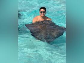 A man enjoys a close encounter with a stingray in crystal-clear waters, showcasing an unforgettable wildlife experience in a tropical paradise.