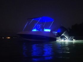 A striking night view of a boat illuminated with blue lights, showcasing its sleek design as it glides through calm waters.