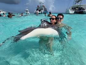 A couple joyfully interacts with a stingray in the crystal-clear waters, showcasing a memorable wildlife experience in a tropical paradise.