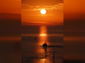 A stunning sunset casts a golden glow over the water as a boat navigates through the tranquil sea, creating a picturesque scene perfect for evening cruises.