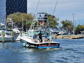 The 'Gunslinger' fishing boat navigates through the harbor with a group of guests onboard, showcasing a lively day on the water.
