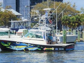 A fishing boat named 'Gunslinger' is seen with a group of people onboard, navigating through the marina — perfect for fishing adventures and group outings.