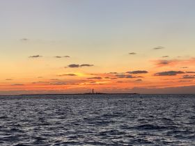 A stunning sunset over the horizon, showcasing a distant island and vibrant colors in the sky — perfect for capturing the beauty of evening boat trips.