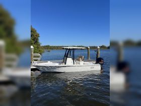 A sleek center console boat docked in calm waters, surrounded by lush greenery and a clear blue sky — perfect for fishing or leisurely outings.