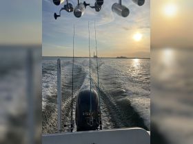 A scenic view from the back of a fishing boat, showcasing the engine and fishing rods against a beautiful sunset backdrop — perfect for fishing enthusiasts.