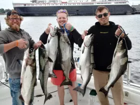 Three friends proudly display their catch of the day while fishing, showcasing a successful outing on the water.