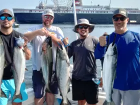 A group of friends proudly displays their impressive catch while fishing on a boat, showcasing a successful day on the water.