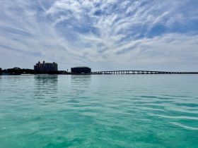 A serene view of the coastline featuring a bridge and buildings under a beautiful sky, perfect for showcasing the tranquil beauty of the area.