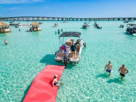 A vibrant scene at a sandbar with guests enjoying the clear waters, swimming, and relaxing on a pontoon boat — a perfect day for fun in the sun.