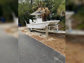 A center console boat parked on a trailer surrounded by lush greenery, showcasing its sleek design and readiness for adventure.