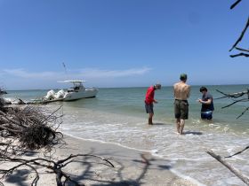 A group of friends enjoys a sunny day at the beach, interacting in the shallow water near their boat — a perfect setting for relaxation and fun on the water.