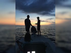 A group enjoys a fishing trip at sunset, silhouetted against the vibrant sky — a perfect moment for bonding and adventure on the water.