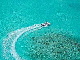 Aerial view of a speedboat gliding through crystal-clear turquoise waters, showcasing the beauty of a tropical paradise.