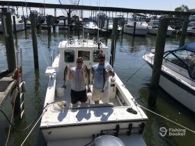 Two anglers proudly display their catch aboard a fishing boat at the marina, showcasing a successful day on the water.