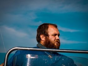 A close-up of a man on a boat, with a focus on his expression against a backdrop of blue skies.