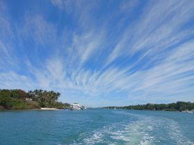A picturesque view of a serene waterway lined with lush greenery and a yacht docked nearby, showcasing the beauty of coastal landscapes.