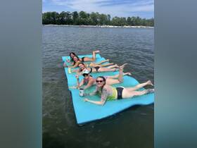 A fun group of friends enjoys a sunny day on a floating mat, sipping drinks and soaking up the sun — perfect for summer parties on the water.