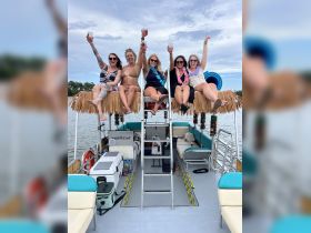 A lively group of friends celebrates on a pontoon boat, raising their cocktails in a fun-filled day on the water.
