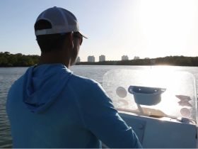 A person navigates a boat while enjoying the scenic view under the bright sun, showcasing the beauty of a day on the water.