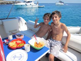 Two boys enjoy a fun snack on a boat, surrounded by clear blue waters — a perfect moment of joy and relaxation on the ocean.