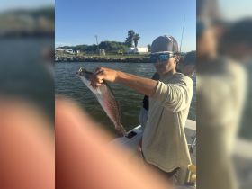 A young angler proudly displays his catch while fishing on a boat, capturing the excitement of a day on the water with friends.