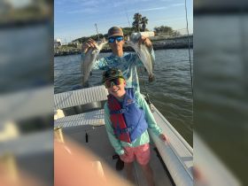 A young boy and a teenager proudly display their catch of the day while fishing on a boat, showcasing a fun family outing on the water.