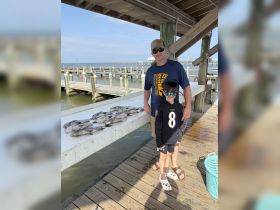 A father and son proudly display their fishing catch on a dock, capturing a memorable moment of family bonding and outdoor adventure.