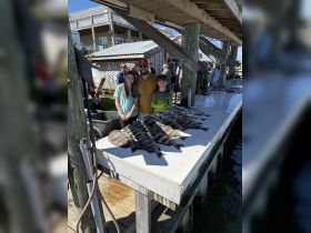 A joyful group of children and an adult pose with their catch of the day at a fishing dock, celebrating a successful fishing trip.