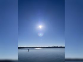 A serene view of the sun reflecting on calm waters, capturing the tranquility of a clear day.