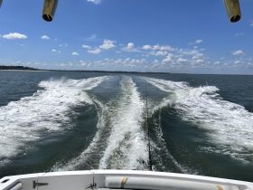 A scenic view from the bow of a boat, showcasing the wake as it moves through the water under a clear blue sky — perfect for boating enthusiasts and adventure seekers.